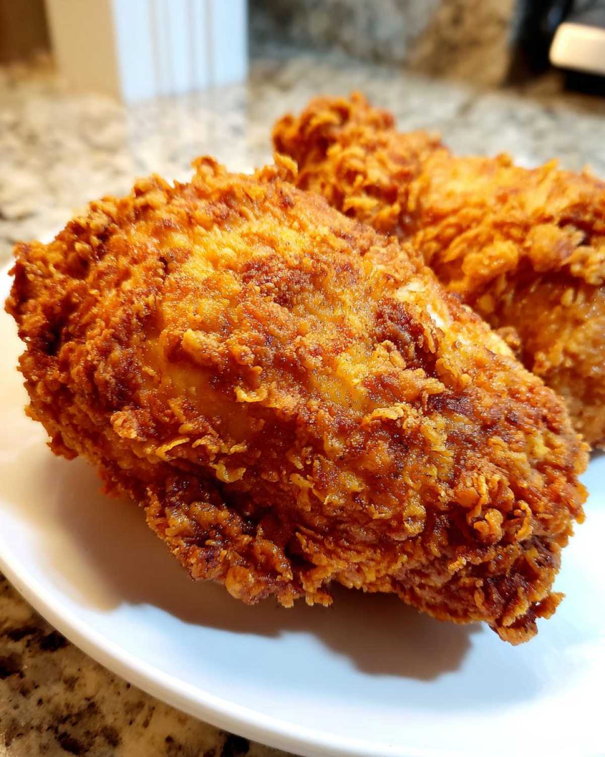 Close-up of two pieces of golden brown, crispy air fryer fried chicken on a white plate.