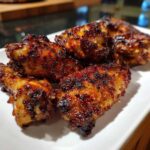 Close-up of several glossy, dark-glazed, crispy baked chicken wings piled on a white serving dish.