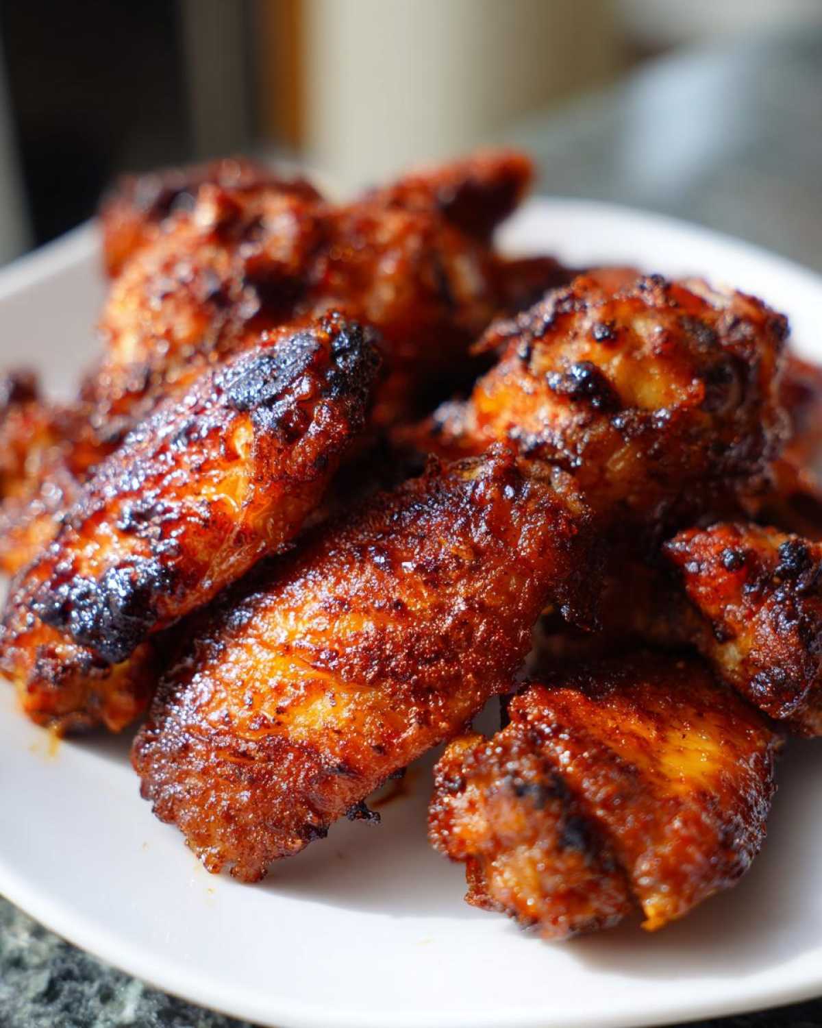 A close-up shot of several perfectly cooked, crispy baked chicken wings piled on a white plate.