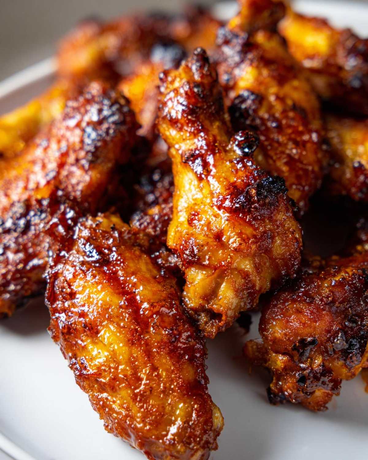 A close-up shot of several glossy, caramelized crispy baked chicken wings piled on a white plate.