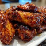 A close-up shot of a pile of glossy, glazed crispy baked chicken wings on a white platter.