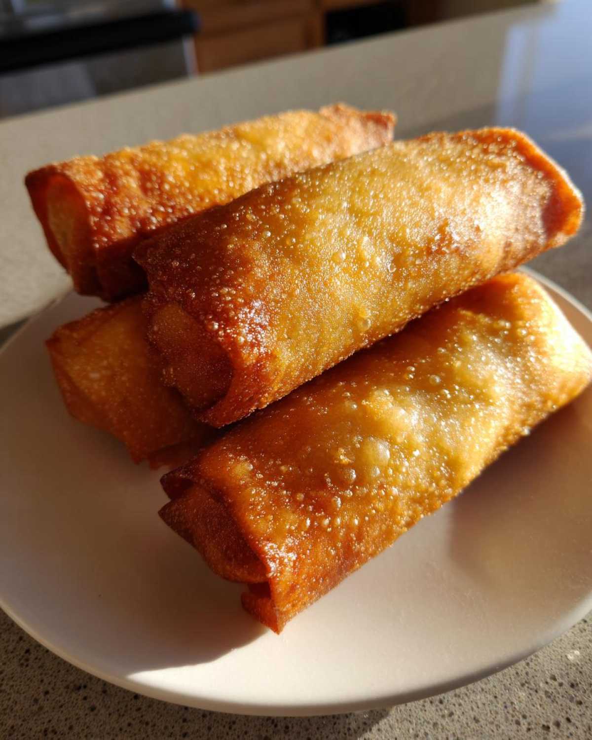 A stack of four perfectly fried, golden brown, crispy egg roll appetizers resting on a white plate.