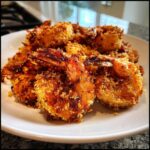 A close-up of perfectly crispy fried shrimp piled high on a white plate, showcasing the golden-brown breading.