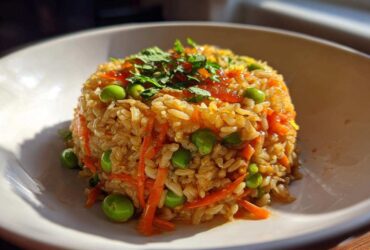 A molded serving of savory crispy rice salad mixed with shredded carrots and bright green peas, topped with herbs.