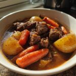 Close-up of a bowl filled with rich crockpot beef stew featuring tender beef chunks, carrots, and potatoes in savory broth.