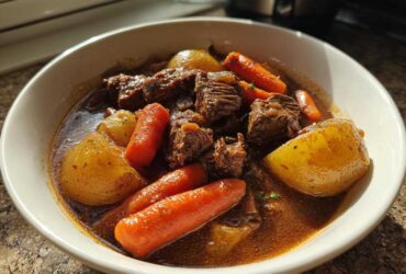 Close-up of a bowl filled with rich crockpot beef stew featuring tender beef chunks, carrots, and potatoes in savory broth.