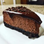 A rich, dark slice of chocolate cheesecake with a thick crust, chocolate ganache, and cookie crumbles on top.
