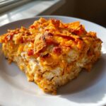 A generous slice of cheesy Dorito Casserole showing layers of shredded chicken and a crunchy, orange Doritos topping.