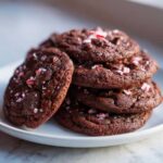 A stack of rich, dark double chocolate peppermint cookies topped with crushed candy canes.