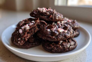 A stack of rich, fudgy double chocolate peppermint cookies topped with chocolate chips and crushed candy canes.