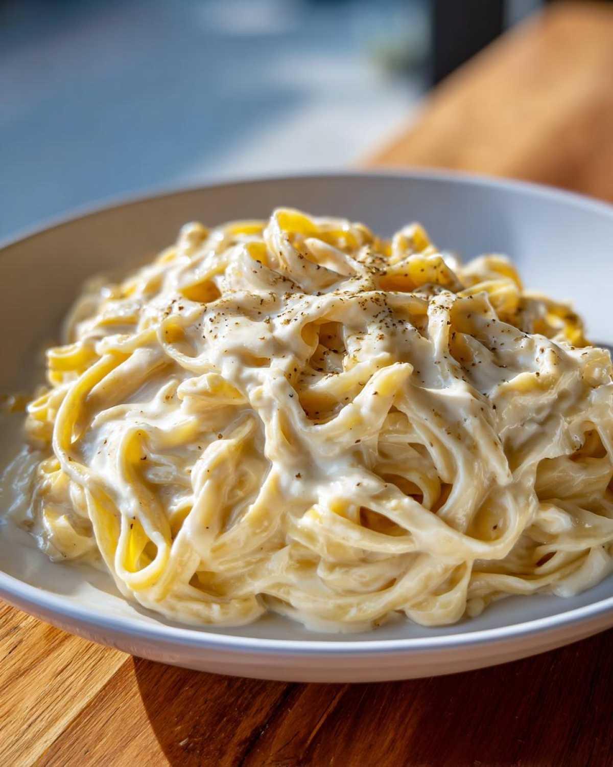 Close-up of fettuccine pasta generously coated in creamy Olive Garden Alfredo sauce and sprinkled with pepper.