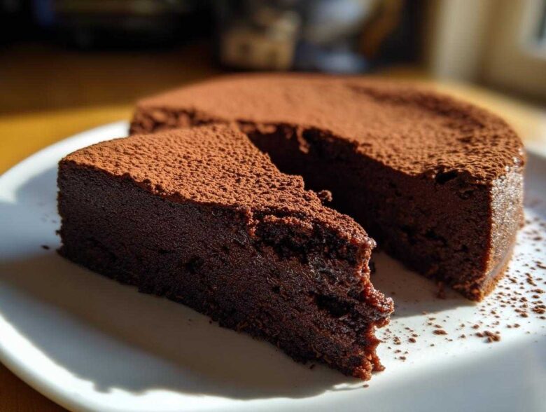 A slice of dense, dark flourless chocolate torte dusted heavily with cocoa powder, sitting next to the main cake.