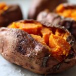 Close-up of a fluffy baked sweet potatoes, split open to show the bright orange interior, sprinkled with coarse sea salt.