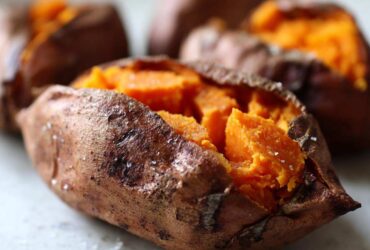 Close-up of a fluffy baked sweet potatoes, split open to show the bright orange interior, sprinkled with coarse sea salt.
