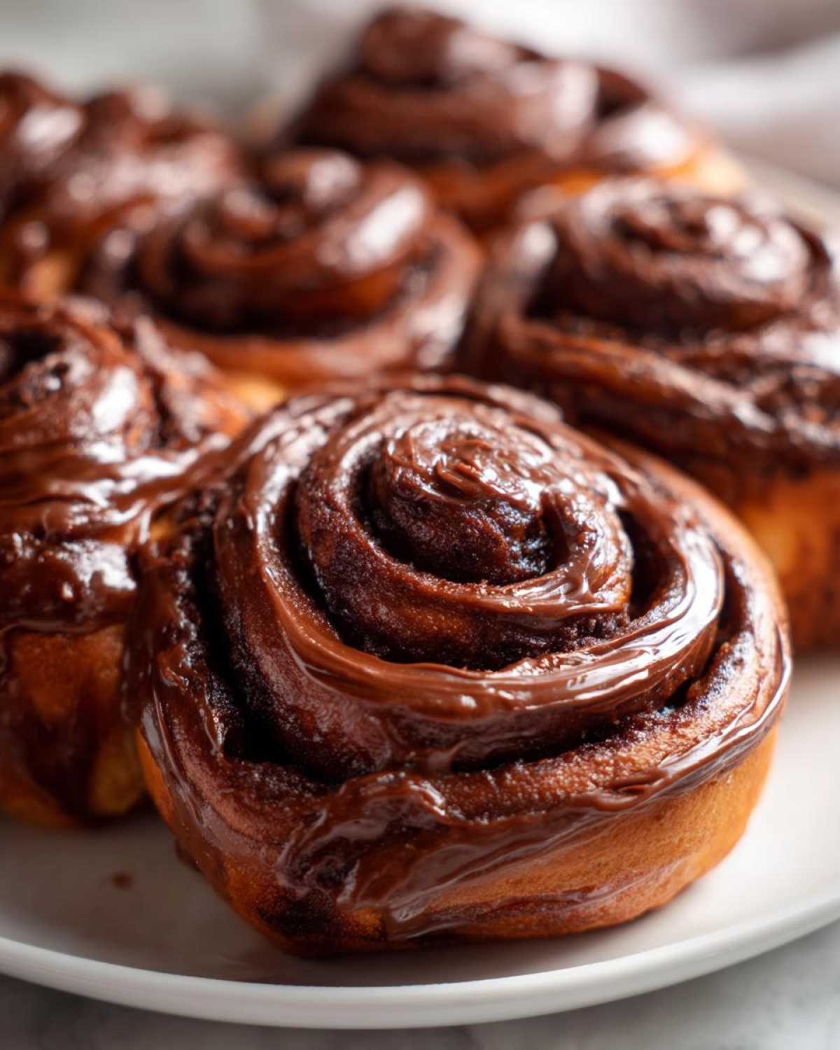 Close-up of several freshly baked chocolate cinnamon rolls covered in rich, glossy chocolate frosting.