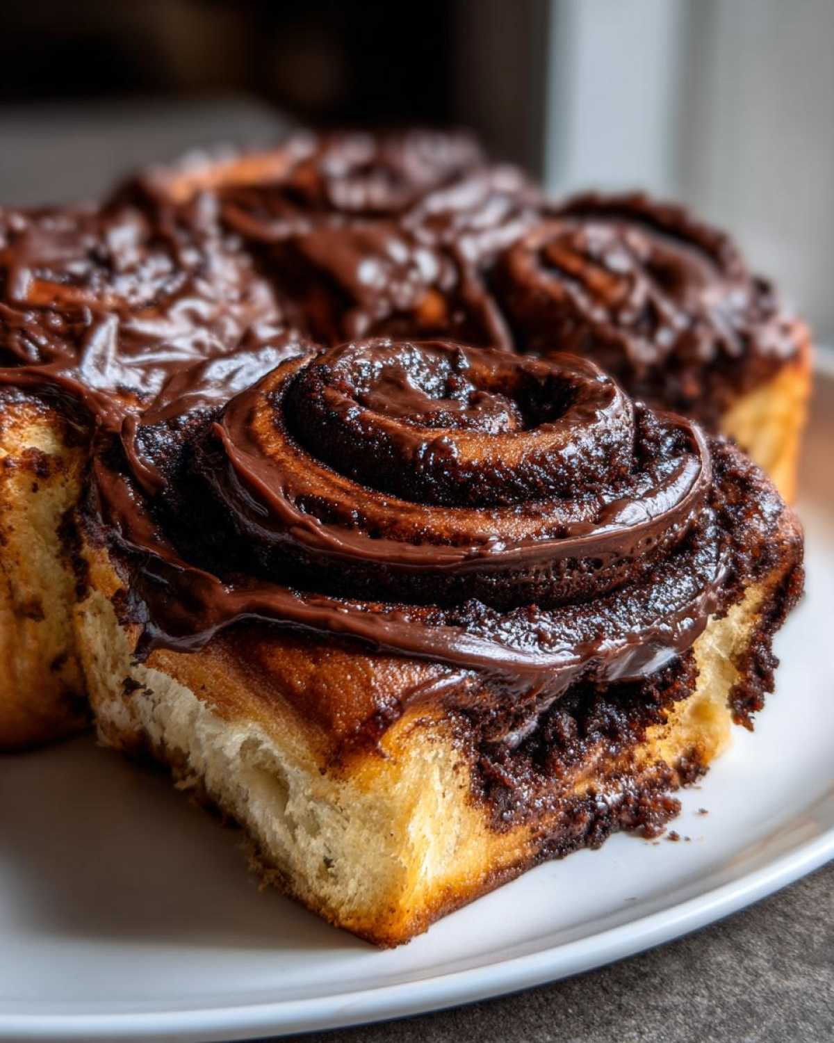 Close-up of a fluffy chocolate cinnamon roll topped with thick, glossy chocolate frosting.