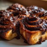 Close-up of fluffy chocolate cinnamon rolls generously topped with a thick, glossy chocolate glaze.
