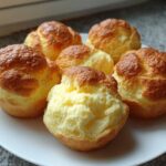 Six freshly baked, golden-brown cloud bread buns displayed on a white plate.