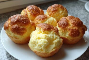 Six freshly baked, golden-brown cloud bread buns displayed on a white plate.