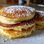 A close-up stack of three fluffy coconut flour pancakes dusted generously with powdered sugar on a white plate.