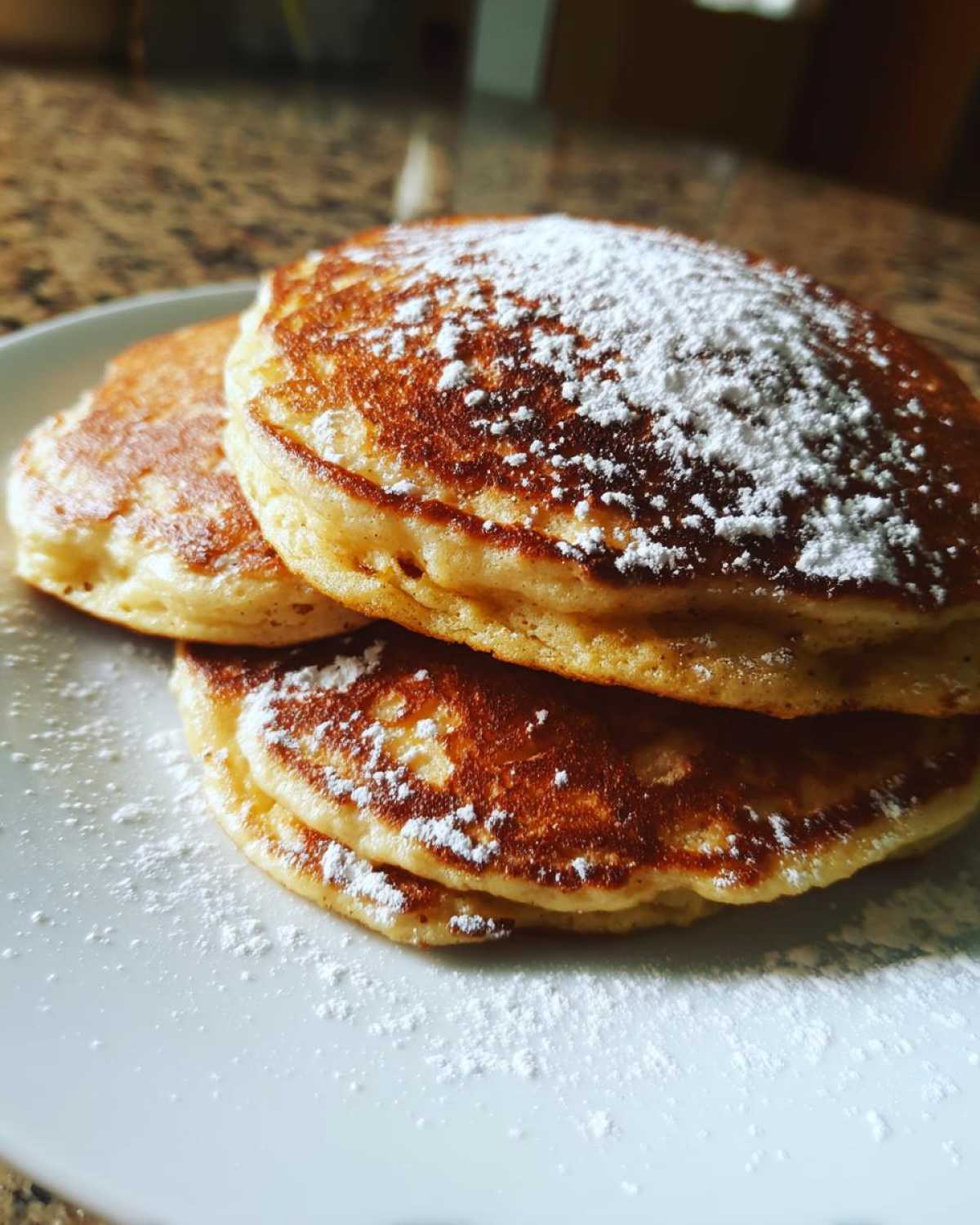 A close-up stack of three golden brown coconut flour pancakes dusted generously with powdered sugar.