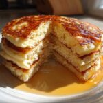 A stack of fluffy greek yogurt pancakes with a piece cut out, drizzled generously with golden syrup.
