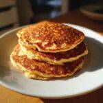 A stack of three perfectly golden brown oatmeal pancakes resting on a white plate.