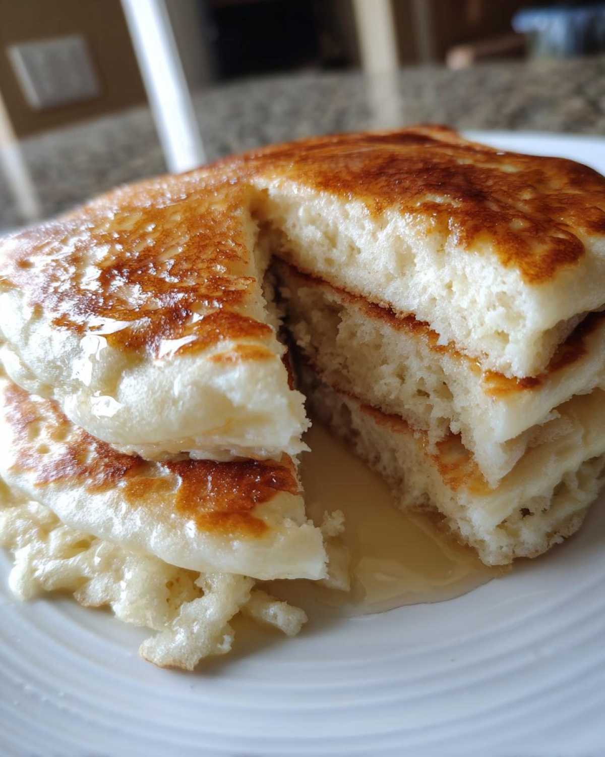 Close-up of a stack of incredibly fluffy pancakes cut open, showing the airy interior and syrup pooling below.