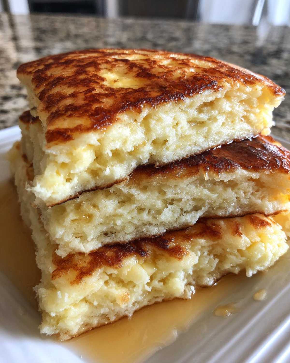 Cross-section view showing the airy interior of three stacked fluffy pancakes drizzled with syrup.
