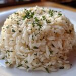 Close-up of a perfectly molded serving of fluffy rice pilaf topped with chopped green herbs.