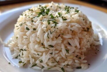 Close-up of a perfectly molded serving of fluffy rice pilaf topped with chopped green herbs.