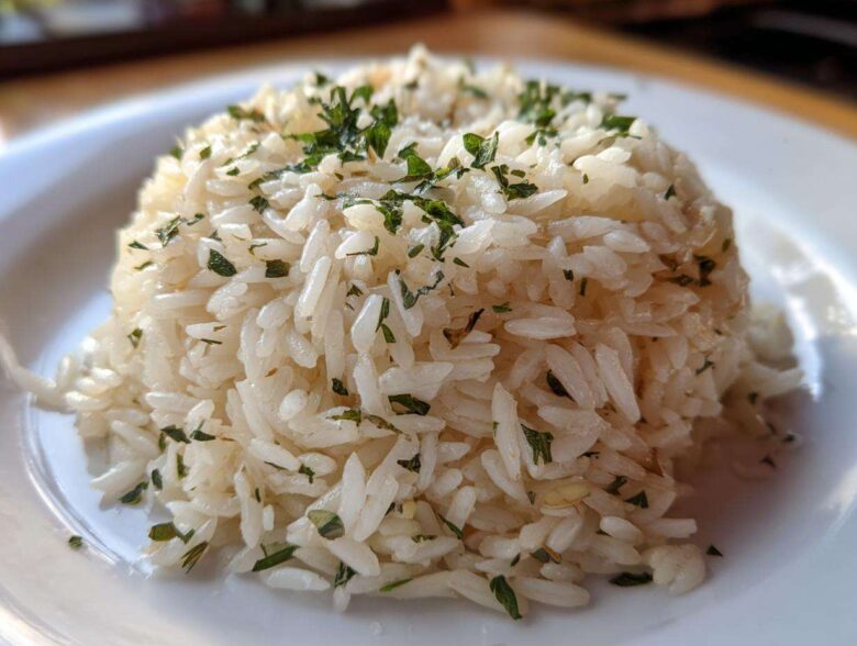 Close-up of a perfectly molded serving of fluffy rice pilaf topped with chopped green herbs.