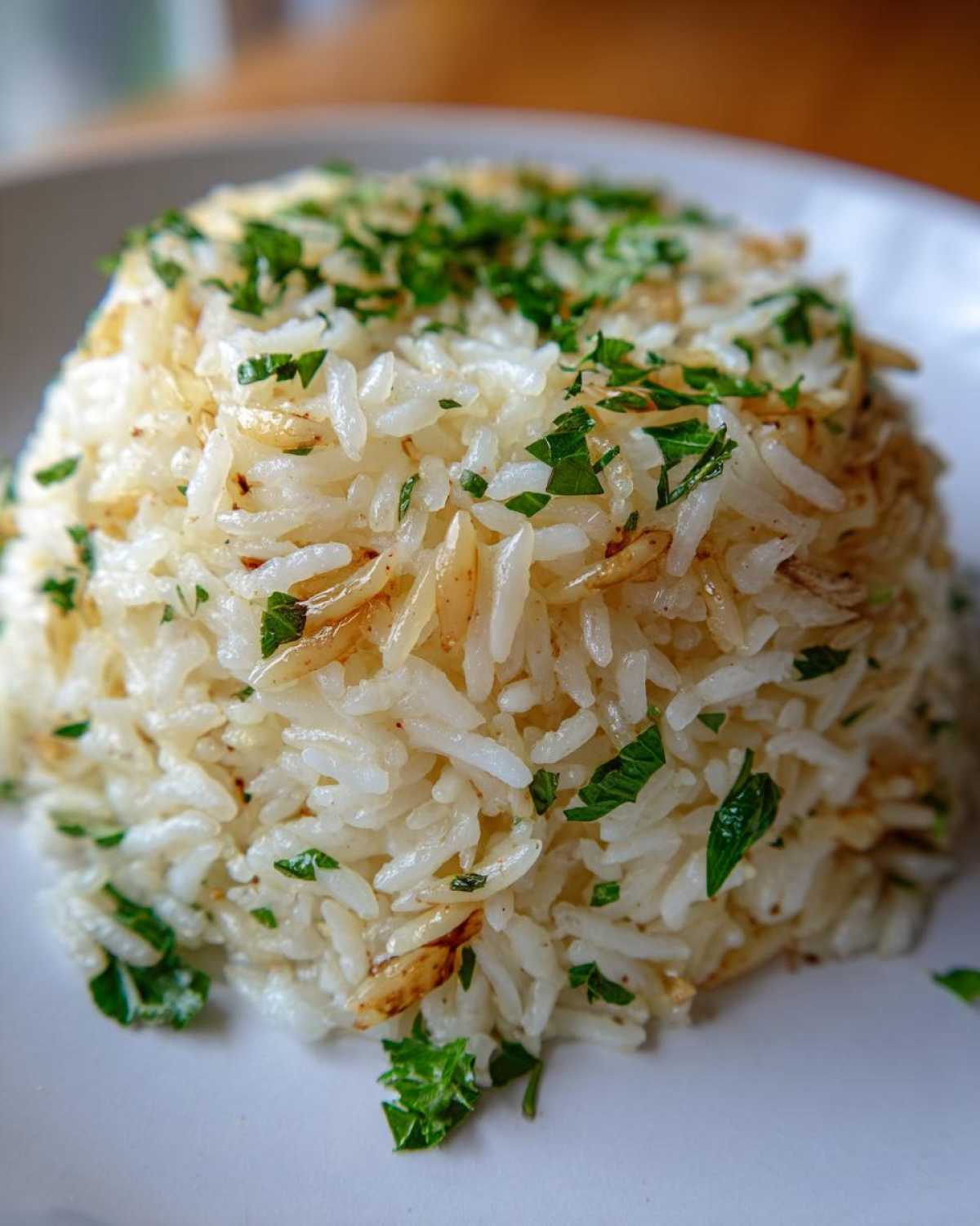 Close-up of a perfectly fluffed mound of white rice pilaf, mixed with toasted grains and topped with fresh chopped parsley.