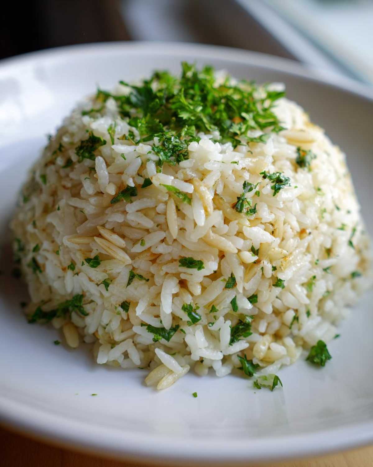 A perfectly molded serving of fluffy rice pilaf garnished generously with chopped fresh parsley.