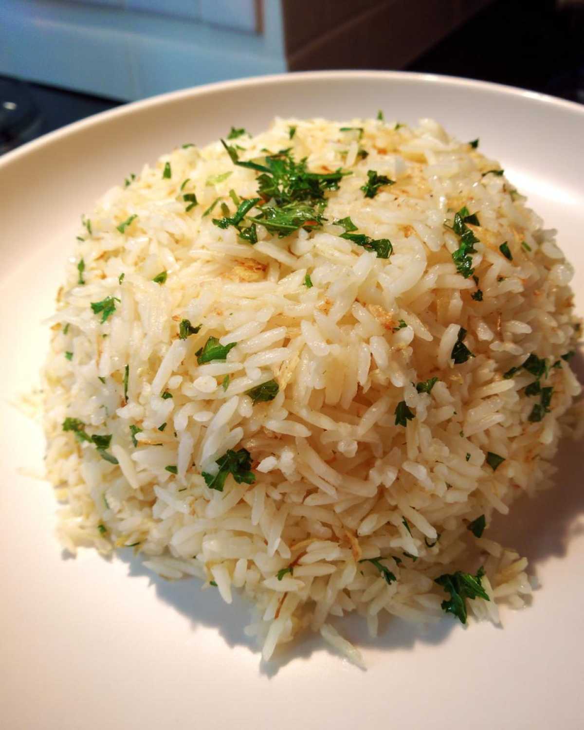 A perfectly molded mound of fluffy rice pilaf garnished with fresh chopped parsley on a white plate.