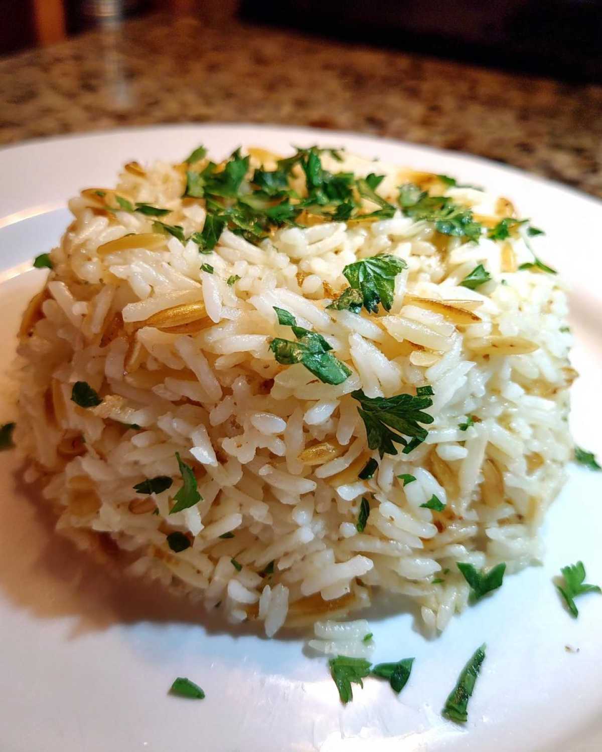 A molded serving of fluffy rice pilaf mixed with toasted vermicelli and topped with fresh parsley.