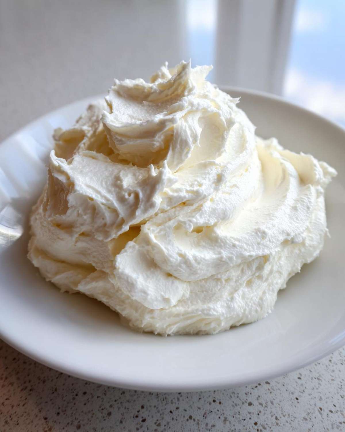 A large swirl of fluffy white vanilla buttercream frosting mounded on a small white plate.