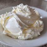 A generous swirl of perfectly whipped vanilla buttercream frosting piled high on a small white plate.