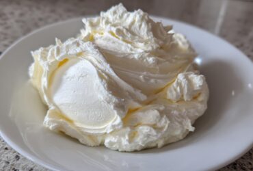A generous swirl of perfectly whipped vanilla buttercream frosting piled high on a small white plate.