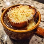 Close-up of a crock of hot french onion soup topped with a toasted crouton and bubbly, melted Gruyère cheese.