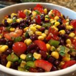 Close-up of fresh cowboy caviar dip featuring black beans, corn, tomatoes, and green peppers in a white bowl.
