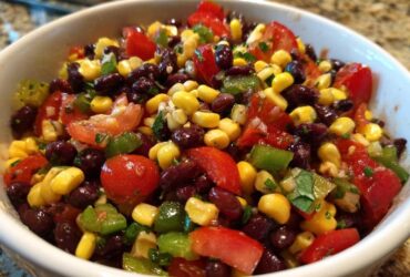 Close-up of fresh cowboy caviar dip featuring black beans, corn, tomatoes, and green peppers in a white bowl.