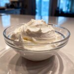 A clear glass bowl filled with thick, white, freshly mixed royal icing recipe.