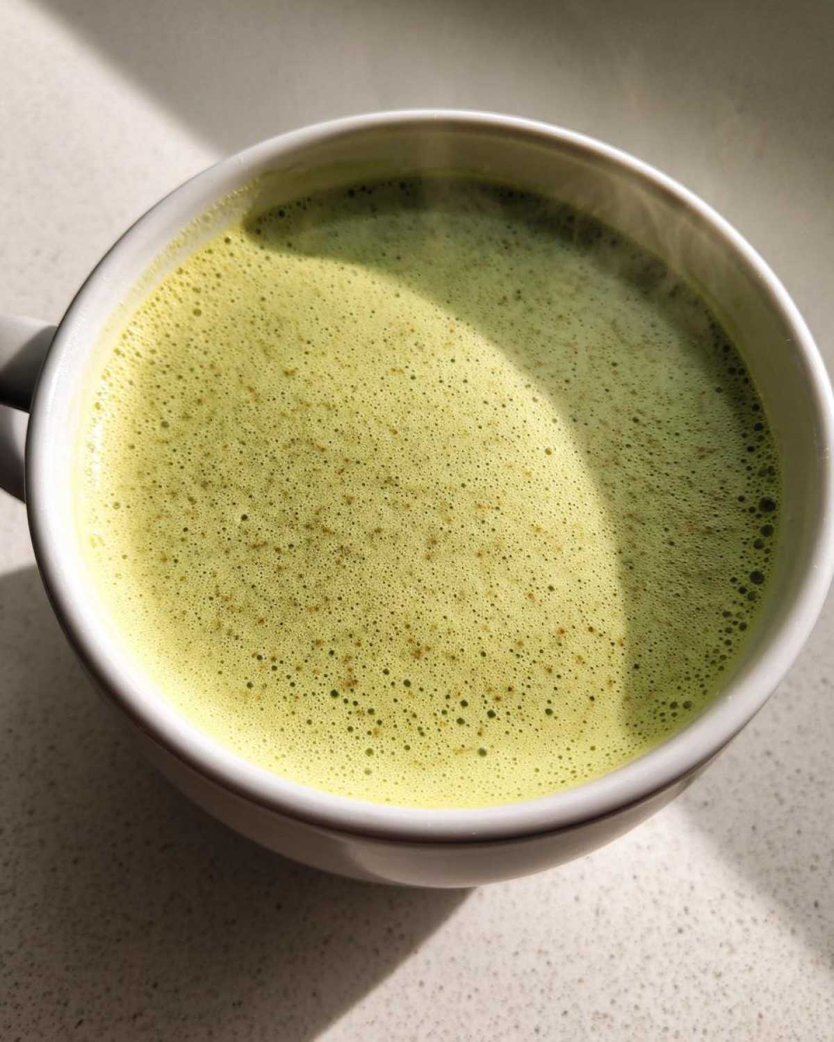 Close-up of a steaming mug filled with frothy, light green celery soup.