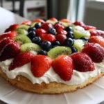 A beautifully decorated fruit pizza sugar cookie topped with whipped cream, strawberries, blueberries, and kiwi slices.