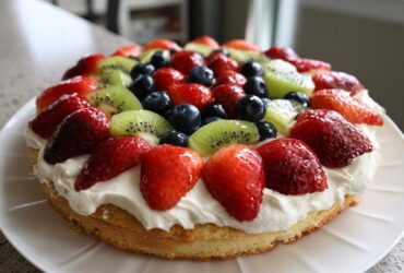 A beautifully decorated fruit pizza sugar cookie topped with whipped cream, strawberries, blueberries, and kiwi slices.