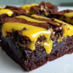 Close-up of a fudgy, dark chocolate Lemon Brownies square topped with a thick, bright yellow lemon glaze drizzle.