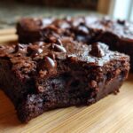 Close-up of a fudgy sweet potato brownies square topped with melted chocolate chips on a wooden board.