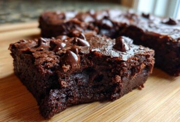 Close-up of a fudgy sweet potato brownies square topped with melted chocolate chips on a wooden board.