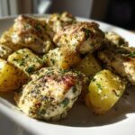 Close-up of juicy garlic parmesan chicken and potatoes seasoned with herbs on a white plate.